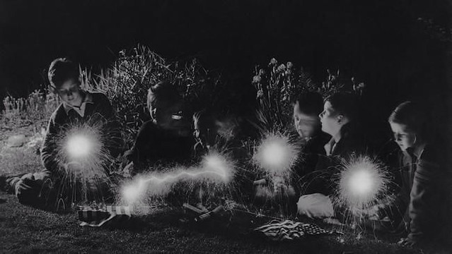 A group of children playing with sparklers after the 4th of July celebrations. 1940
