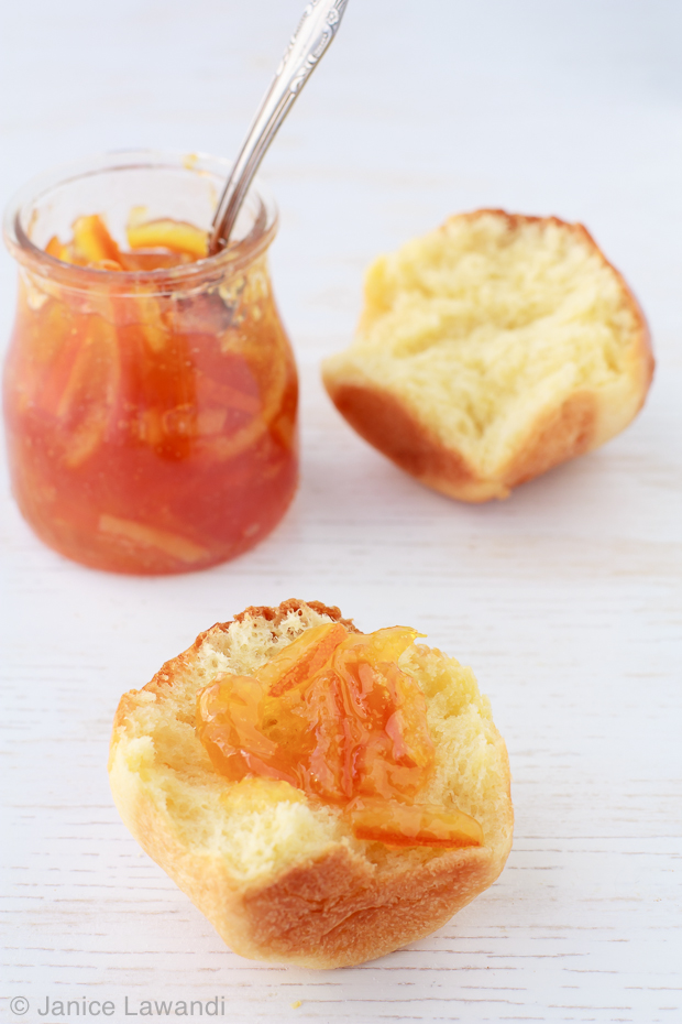 Brioche buns broken open to show fluffy interior served with homemade marmalade in a small jar with a silver spoon.