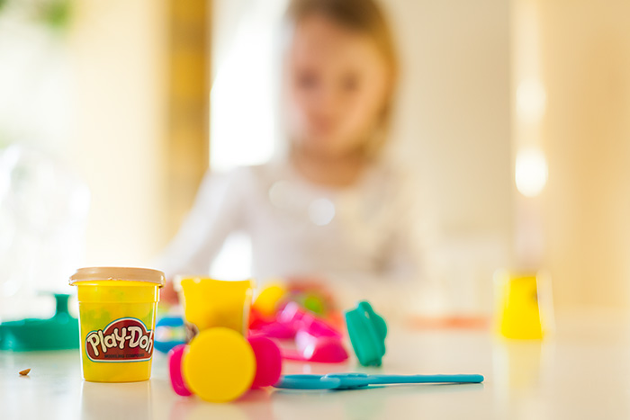 A Can of play-doh surrounded by play-doh tools and a child in the background.
