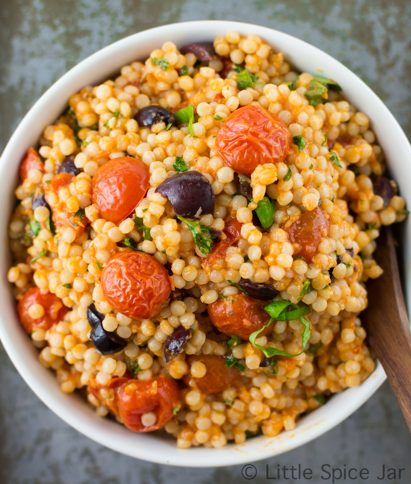 roasted vegetable pearl couscous salad in white bowl with wooden spoon