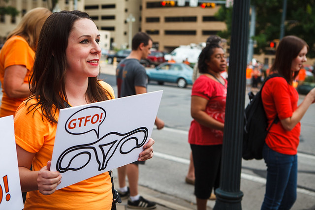 A pro-choice protester holds a sign with a uterus saying "GTFO!"