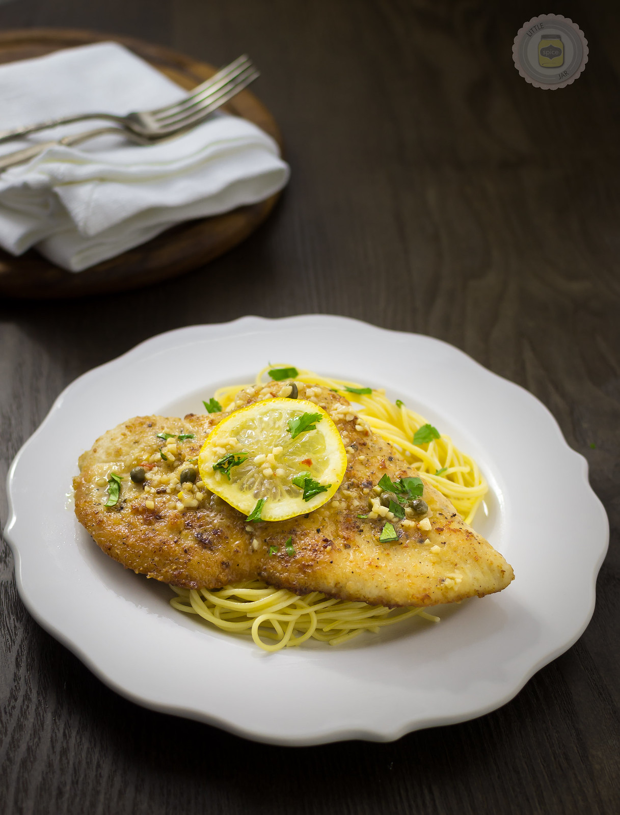 plate with prepared spaghetti topped with chicken breast with lemon slice and parsley