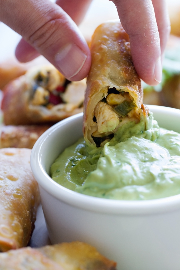 hand dipping cut egg roll in avocado sauce