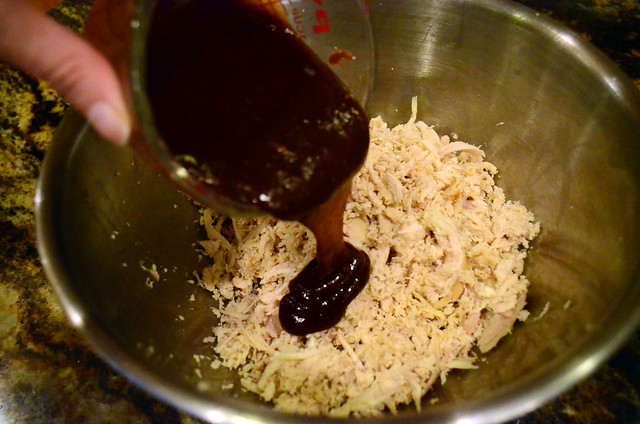 A bowl of shredded rotisserie chicken with barbecue sauce being poured on top.