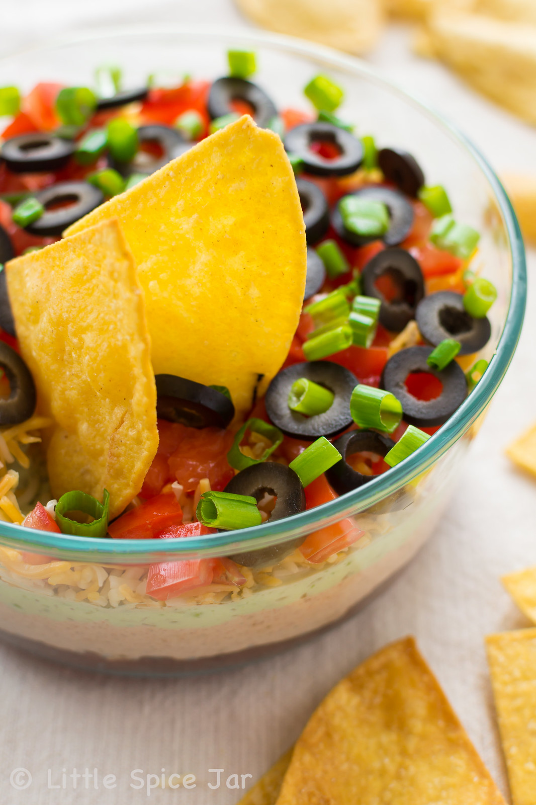 seven layer dip on glass bowl surrounded by homemade tortilla chips