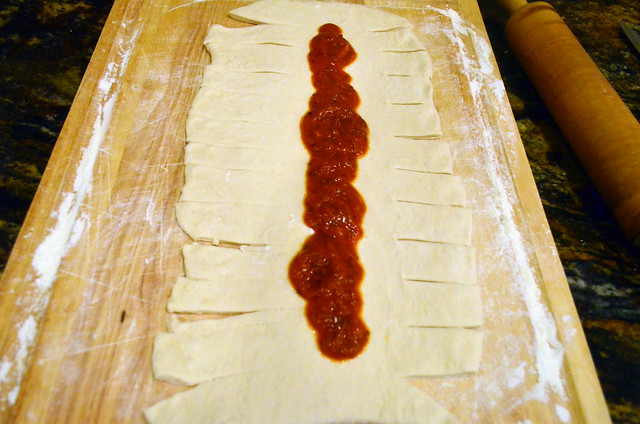 Sliced dough with marinara sauce poured across the center of the dough.