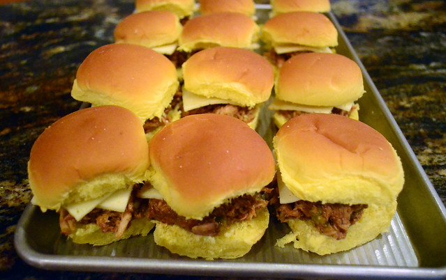 Several assembled barbecue chicken sliders arranged on a rimmed baking sheet.