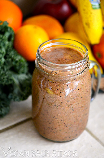 Speckled strawberry smoothie in a jar, in front of fruit and kale