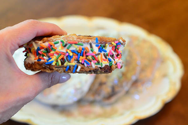 A hand hold Ice cream that is sandwiched between two cookies with sprinkles on the sides.