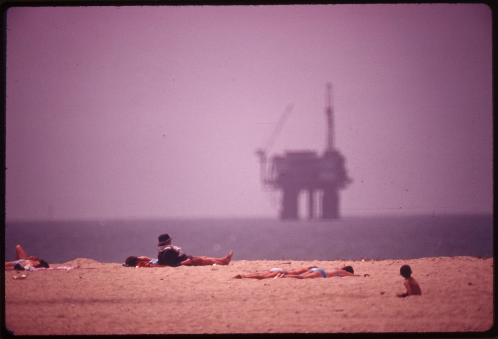 Sunbathers at Huntington Beach, and an oil platform offshore, May 1975