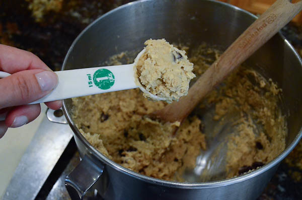 A measuring spoon is spooning out cookie dough from the stand mixer bowl.