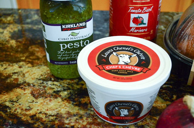 A container of goat cheese and a jar of pesto sauce.