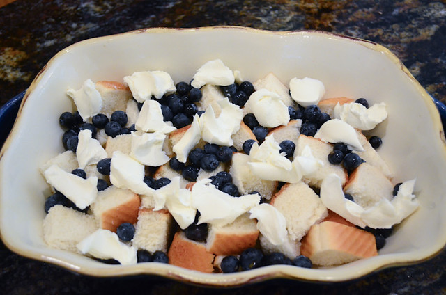 Dollops of mascarpone cheese and fresh blueberries on top of the bread cubes in a casserole dish.