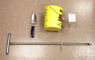 Picture soil sampling equipment - a soil probe, a hand shovel, a bucket, and a bag with a label.