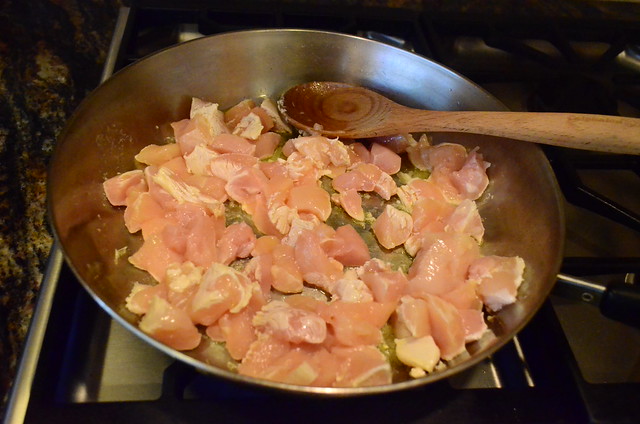 A large pan with cut up chicken cooking on a stove top.