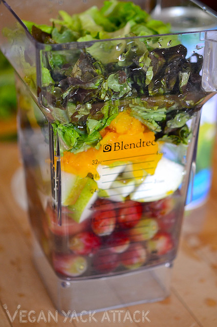 blender pitcher filled with grapes, pear, pumpkin, and greens