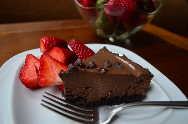 A slice of the chocolate pudding tart with sliced strawberries on the side.