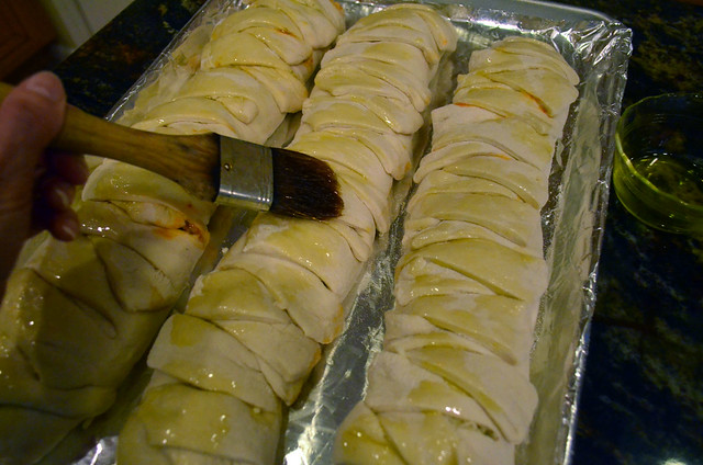 Three uncooked calzones on a foil lined baking sheet being brushed with olive oil.