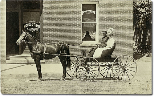horses people woman usa signs man men history sepia buildings advertising clothing women hats indiana transportation shops storefronts buggy buggies businesses huntingburg realphoto duboiscounty hoosierrecollections