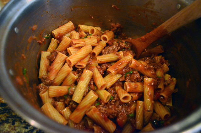 A wooden spoon stirs the rigatoni with meat sauce.