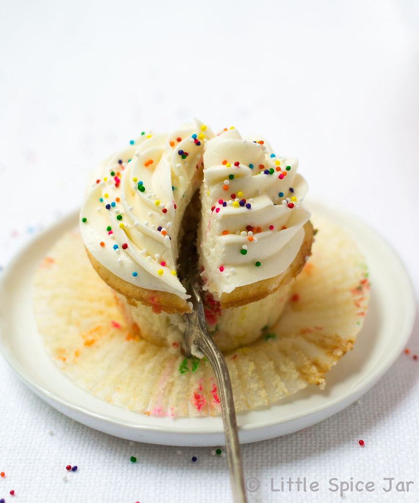 cupcake on white plate with sprinkles on top sliced with fork 
