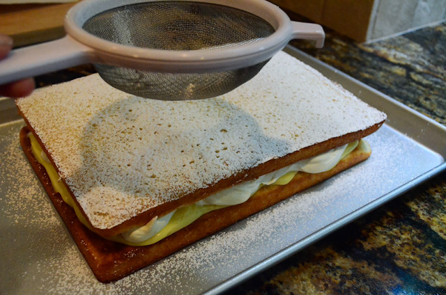 Confectioners' sugar is being sprinkled through a strainer on top of the cake.