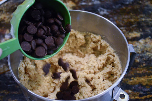 Dark chocolate chips are poured into the stand mixer with a measuring cup.