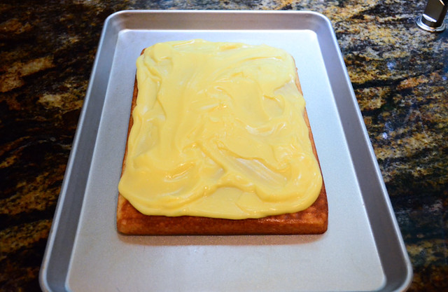 The cake placed on a large baking sheet with vanilla pudding spread across the top of the cake.