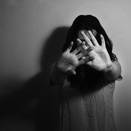 Black and white photo of a person with long dark hair holding their arms straight out towards the camera, with palms facing outward protectively.