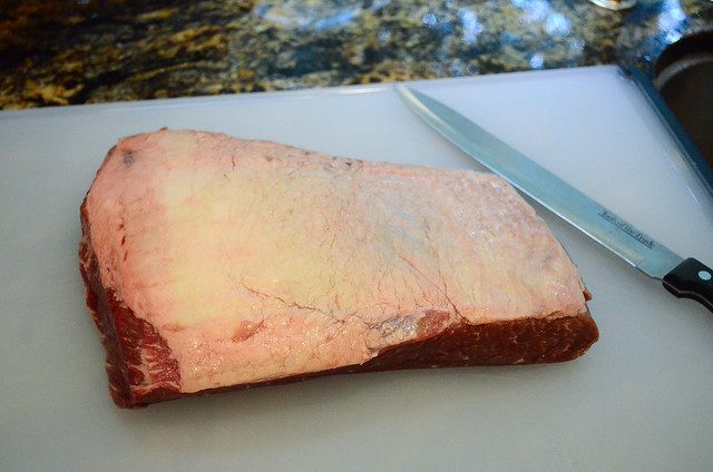 Beef brisket sitting on a cutting board showing the side with a thick layer of fat.