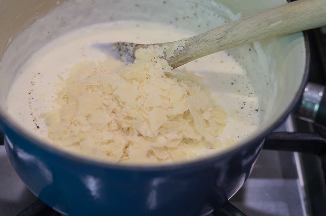 Parmesan is added to a cream sauce in a saucepan.