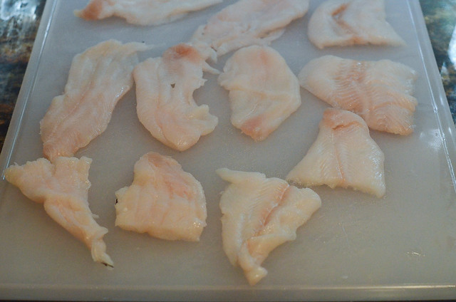 Pieces of raw fish on a plastic cutting board.