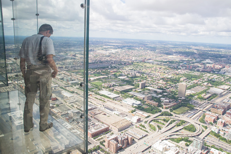 a boy looks out from the transparent balcony of th willis tower