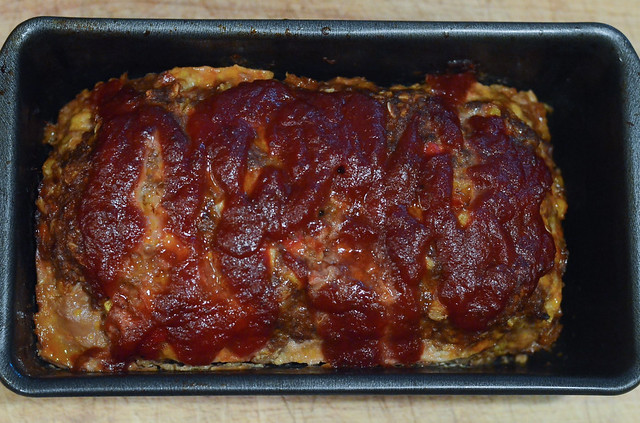 A close up of food glazed meatloaf in a loan pan on a wood board.