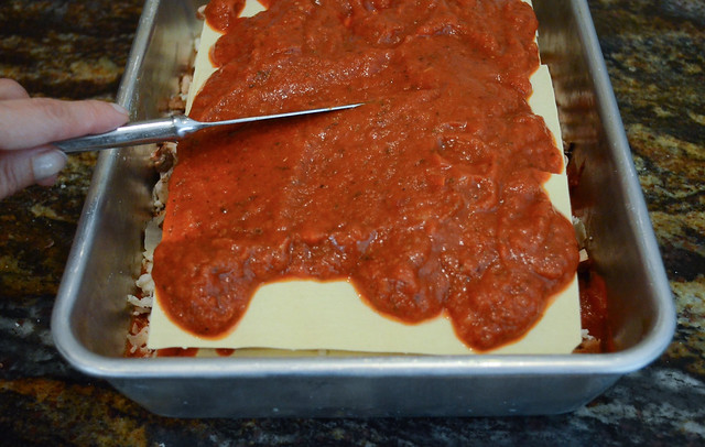 Marinara is added to the final sheet of lasagna sheets and is spread with a knife.