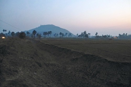 An unlined channel running by tilled fields with a mountain in the background