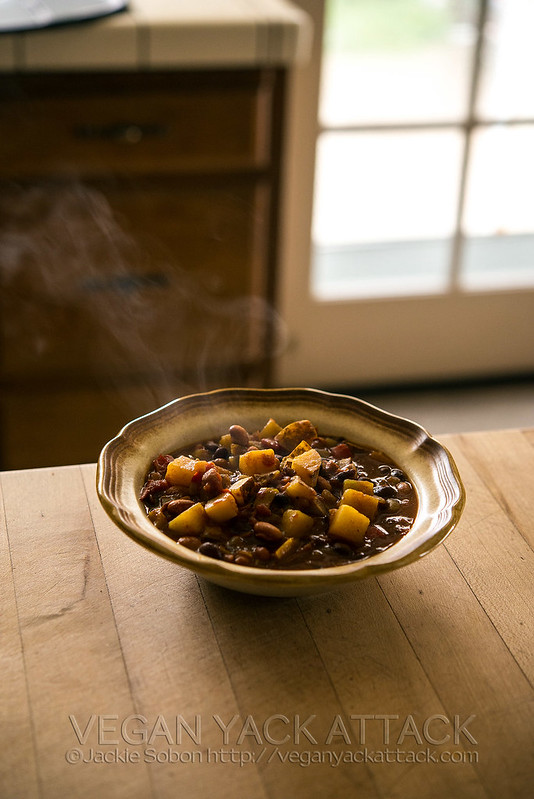 Slow Cooker Potato Curry Chili in a stoneware bowl on a wood table with steam coming out