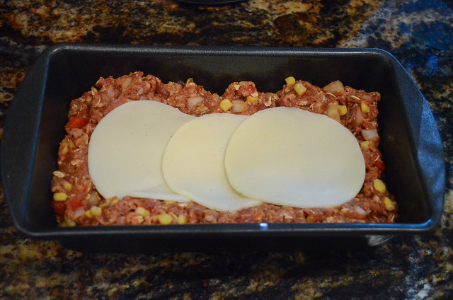 Cheese is layered on to raw meatloaf mixture in a loaf pan.