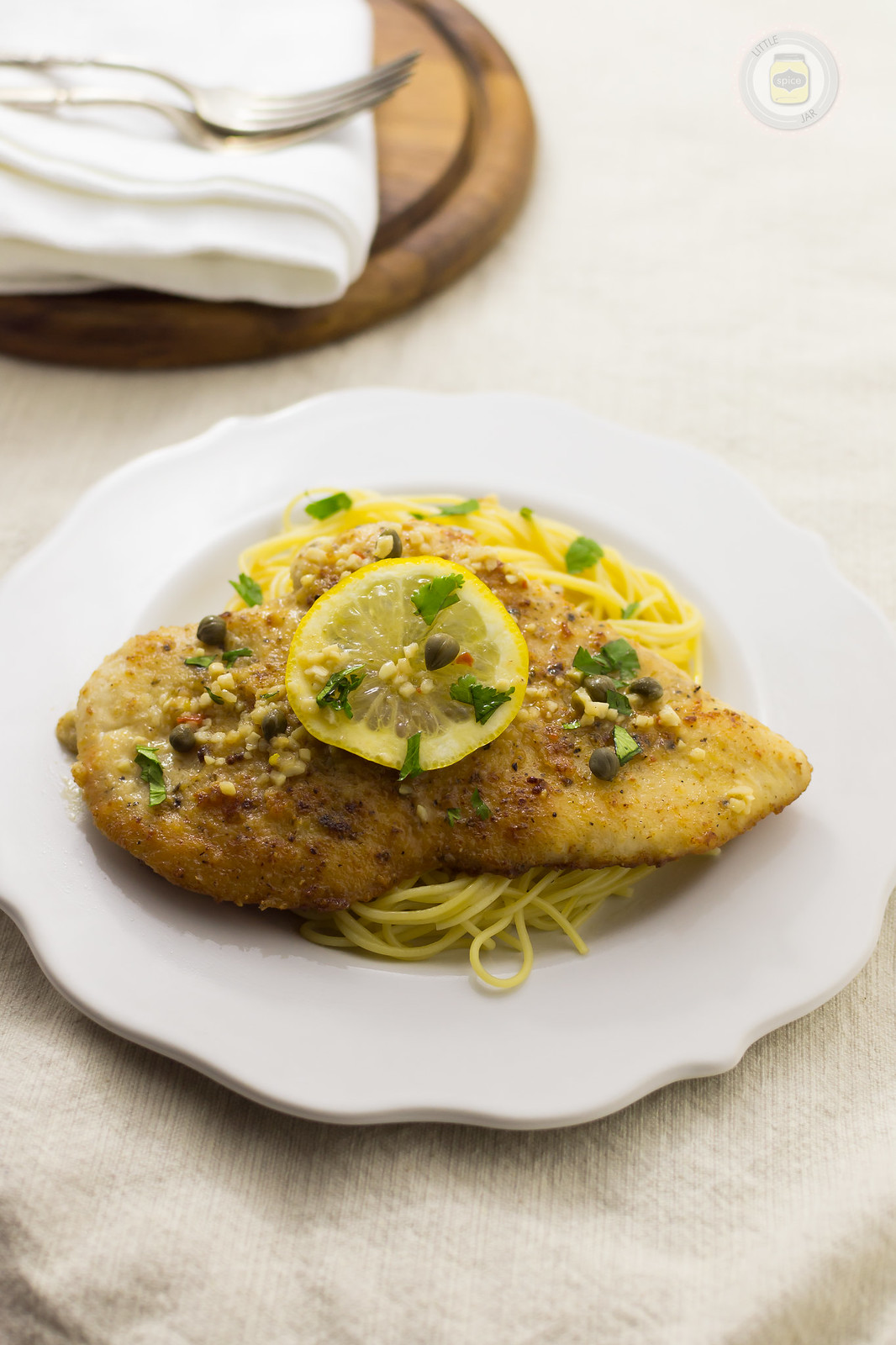 prepared spaghetti and seared chicken with lemon slice and parsley on top on white surface