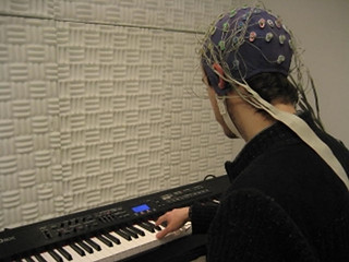 The image shows a person playing a keyboard while wearing an EEG.