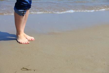 Woman feet with red pedicure relaxing on sand