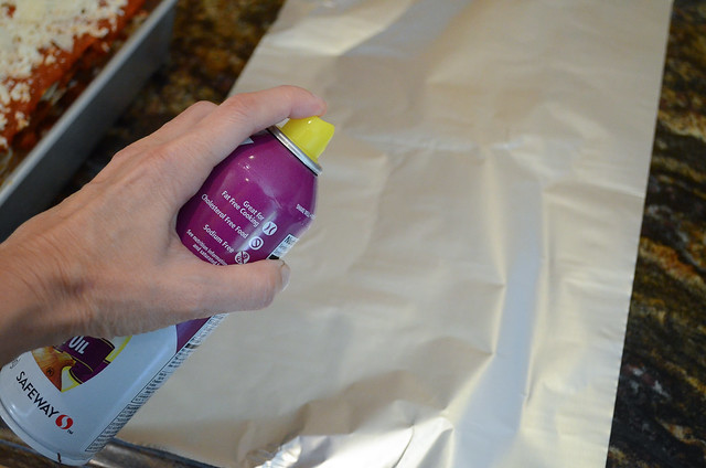 A sheet of foil being sprayed with cooking spray.