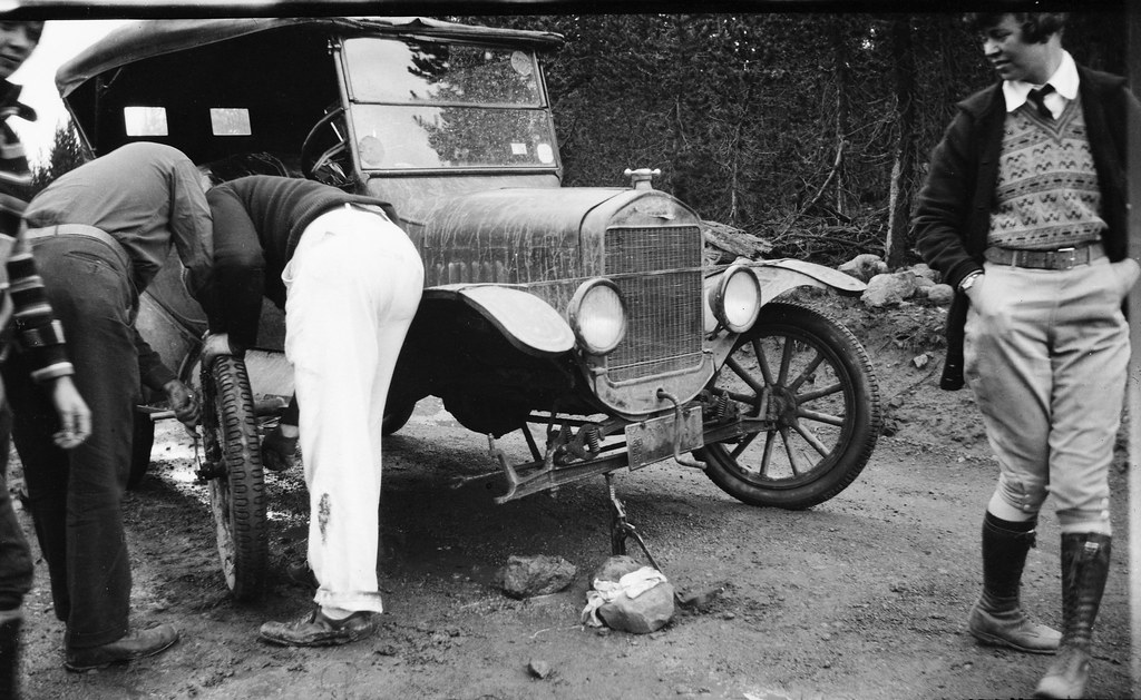 Woman watches as men change a tire on a Model T
