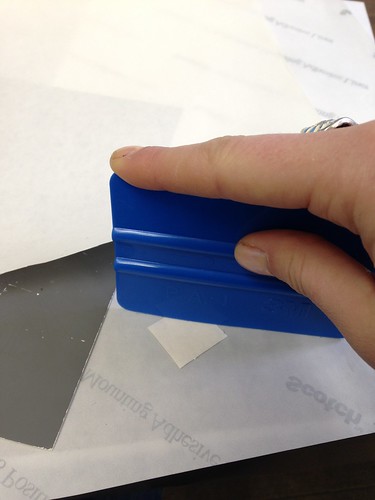 Photograph of plastic squeegee pressing adhesive onto an old label. 