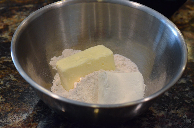 A metal mixing bowl with dry ingredients, butter and cream cheese.