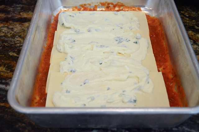 Lasagna sheets are laid across the marinara with ricotta mixture spread on top of the noodles.