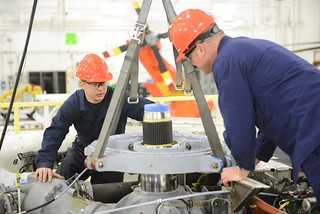 Petty Officers 2nd Class Terry Edington (left) and John Chain, aviation maintenance technicians at Air Station Elizabeth City in North Carolina, lower a new swashplate onto the main gear box of an MH-60 Jayhawk helicopter at the air station Nov. 14, 2014. AMTs like Edington and Chain throughout the Coast Guard are responsible for inspecting, servicing, maintaining, troubleshooting and repairing aircraft engines and systems. (U.S. Coast Guard photo by Petty Officer 3rd Class Nate Littlejohn)