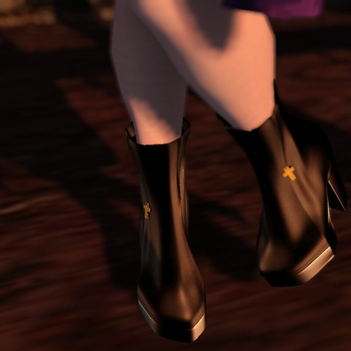 Image Description: Closeup of feet wearing dark brown boots with gold crosses on them, standing on a red carpet.