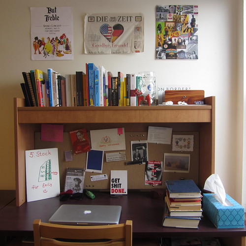 Emily's desk, with neatly stacked books, a MacBook computer, and a bulletin board.