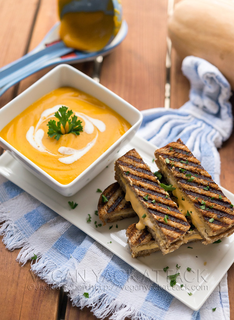 Square white bowl with bright orange butternut bisque inside, with grilled cheese sticks on the side